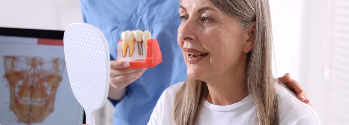 Patient smiling at an implant model in a hand mirror